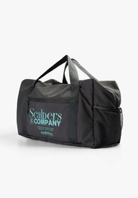 Bolsa de viaje negra con dos asas, bolsillo frontal con texto turquesa "Scalpers Company" y bolsillo lateral de malla.