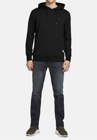 Zwarte hoodie met een voorzak, verstelbare koordjes, geribde manchetten en zoom. Gecombineerd met donkerblauwe jeans en grijze sneakers.