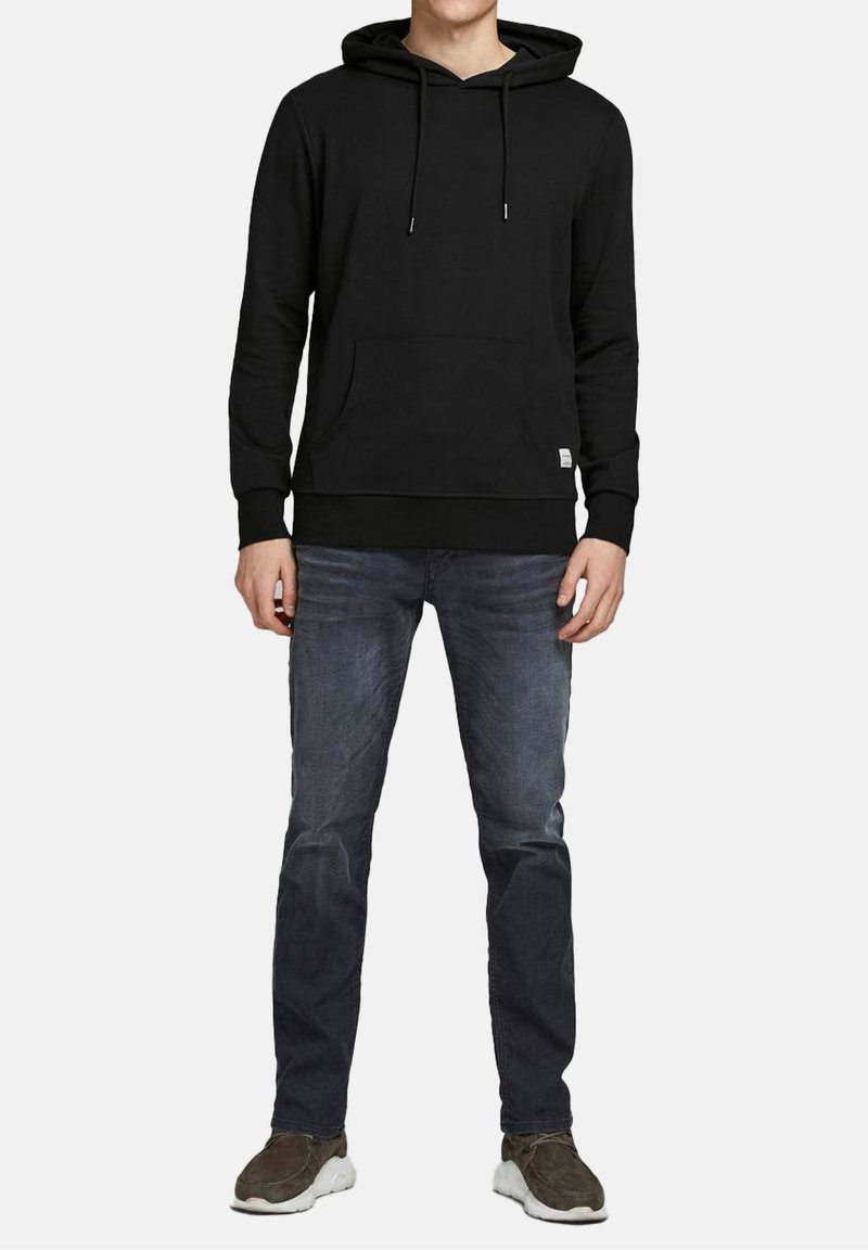 Zwarte hoodie met een voorzak, verstelbare koordjes, geribde manchetten en zoom. Gecombineerd met donkerblauwe jeans en grijze sneakers.