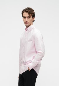 Gaiši rozā garām piedurknēm pogājamā krekla, kas izgatavots no kokvilnas, ar klasisku apkakli, noapaļotu apakšmalu un mazu logotipu uz krūts.