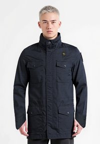 Granatowa kurtka z wysokim kołnierzem, czterema kieszeniami z przodu i zapięciami na zatrzaski. Wykonana z wytrzymałego materiału o lekko teksturowanym wykończeniu.