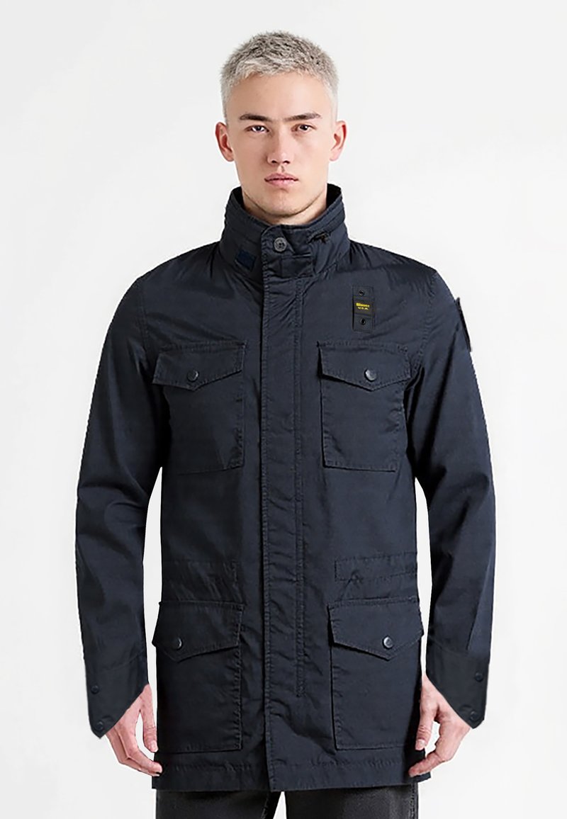 Námořnická modrá bunda s vysokým límcem, čtyřmi předními kapsami a patentními knoflíky. Vyrobena z pevné tkaniny s mírně texturovaným povrchem.