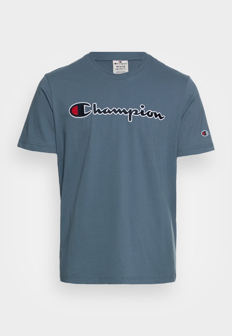 T-shirt à manches courtes et col rond en coton bleu avec un logo "Champion" brodé en noir et rouge sur la poitrine.