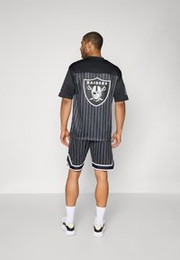 Black basketball jersey and shorts set featuring vertical white stripes, a Raiders logo on the back, and white accents on the shorts.