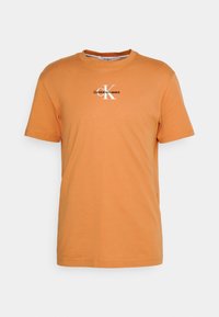 Oranžové bavlněné tričko s kulatým výstřihem. Na hrudi má černobílou potisknutou logo "Calvin Klein Jeans". Krátké rukávy.