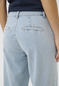Light blue denim jeans with back pockets, featuring a straight cut and a soft texture. Detailed stitching along the pocket edges.