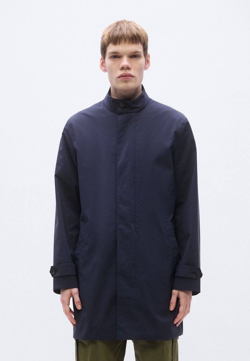 Navy waterproof coat with a high collar, front button closure, and side pockets; features a smooth texture and minimalist design.