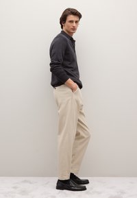 Dunkelgraues Poloshirt mit langen Ärmeln, beige hoch taillierte Hosen und schwarze Loafer. Minimalistisches Design mit leichter Textur und taillierter Silhouette.