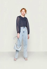 Blusa azul-marinho transparente com riscas verticais, jeans de cintura alta em lavagem clara e uma mala azul-clara com detalhes em corrente. Sandálias com tiras completam o visual.