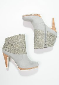 Gray ankle boots with lace detailing around the upper, cork heel, and side zipper. Smooth texture with a sleek, modern design.