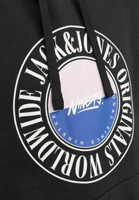 Sweat à capuche noir avec logo circulaire Jack & Jones Originals en blanc, rose et bleu, comportant le mot "Ninety" au centre et des cordons de serrage épais noirs.