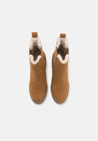 Botas de tobillo de ante color beige con un suave forro de piel sintética, una tira en la parte posterior para facilitar el calzado y costuras en contraste alrededor de la suela.