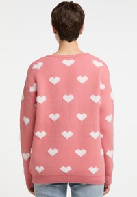 Roher Pullover in Rosa mit weißen Herzmustern, aus weichem, strukturiertem Stoff. Mit Rundhalsausschnitt und gerippten Bündchen. Lockerer Schnitt, lässiges Design.