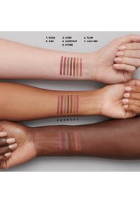 Campioni di sette colori di rossetto su tre diverse tonalità di pelle: chiara, media e scura. I colori includono prugna, castagna e rosso metà.