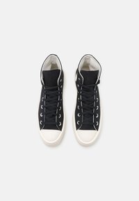 Zapatillas altas negras de lona, con punteras y cordones de goma blanca, ojales plateados y una parte superior texturizada negra.