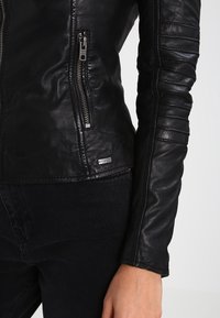 Černá kožená bunda s přiléhavým střihem, s diagonálním zipem, žebrovanými akcenty na rukávech a malou značkovou nášivkou poblíž spodního okraje.
