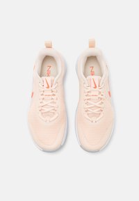 Nike sneakers med en lys ferskenfarvet mesh-overdel, hvid sål og orange detaljer. Har snørelukning og en pull-tab ved hælen.