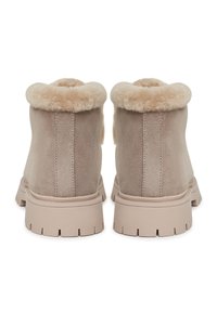 Bottes chelsea en suede beige avec un col doublé en fourrure doux, dotées d'une semelle épaisse et texturée pour l'adhérence et la durabilité.
