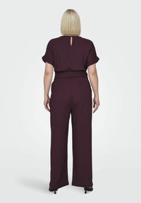 Burgundský overal so krátkymi rukávmi, širokými nohavicami a opaskom v páse. Detaily v tvare kľúčovej diery na chrbte a textúrovaná tkanina.