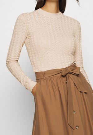 Maglione a maniche lunghe di colore rosa chiaro, lavorato a maglia, con motivo a zigzag testurizzato e scollo rotondo, abbinato a una gonna marrone a vita alta con fiocco e bottoni.
