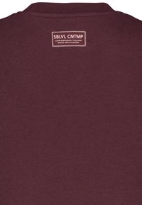 Burgundy cotton sweatshirt with a crew neck, featuring a rectangular label stitched at the back with white text and border.