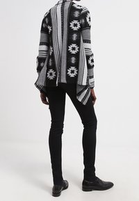 Černobílý cardigan s asymetrickým lemem, stylizovaný s přiléhavými černými kalhotami a černými botami. Texturovaná pletenina a volný střih.