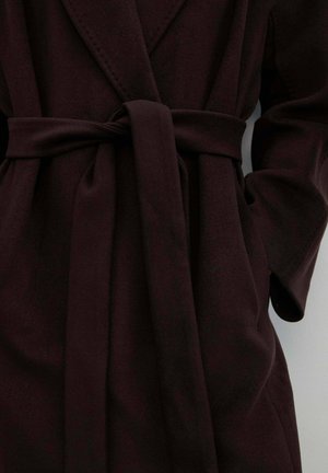 Ciemnobordowy płaszcz kopertowy z paskiem, kołnierzem z klapami i dwoma bocznymi kieszeniami, wykonany z miękkiego, teksturowanego materiału.