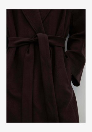 Donker bordeauxrood overslagjack met riem, opstaande kraag en twee zijzakken, gemaakt van een zachte, gestructureerde stof.