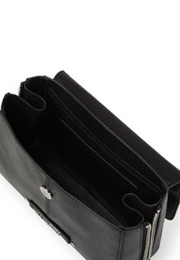 Sac en cuir noir avec fermeture éclair, comportant un intérieur divisé en compartiments et emplacements pour cartes. Texture lisse avec des accents métalliques.