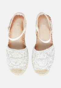 Scarpe espadrillas bianche intrecciate con una cinghia, caratterizzate da una tomaia texturizzata e una punta in cotone beige. Sottopiede di color naturale.