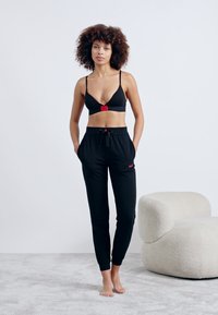Black bralette with a red logo patch, paired with black jogger pants featuring an adjustable waistband and embroidered detail.