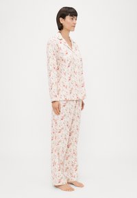 Conjunto de pijama floral composto por uma blusa de mangas longas e calças largas. Feito de um tecido leve com um fundo branco e padrões florais em rosa.
