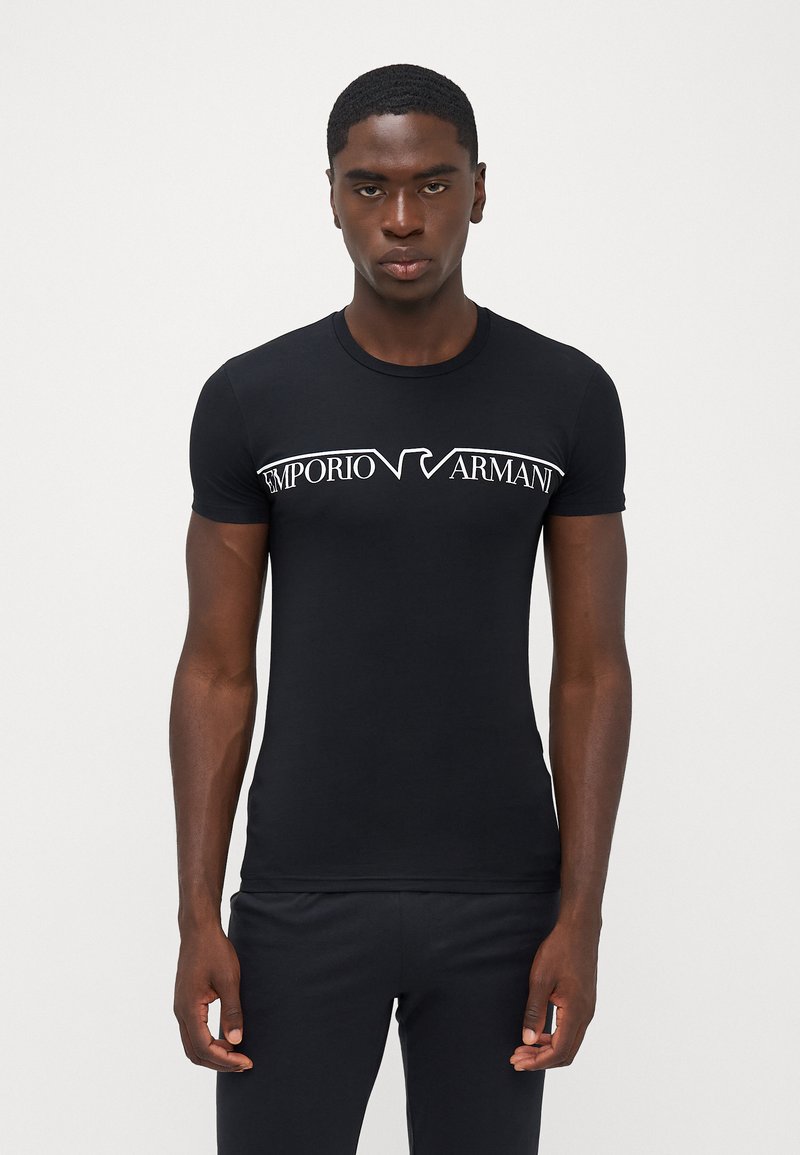 Melna īsās piedurknes T-kreklu, izgatavots no gludas kokvilnas, ar baltu "Emporio Armani" logo krūšu daļā modernā fontā. Pieguļoša piegriezuma.