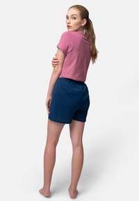Roze hemd met korte mouwen gecombineerd met donkerblauwe, gestructureerde shorts. Het model staat zijwaarts en toont de achterkant van de outfit.