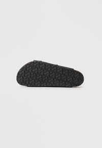Semelle de chaussure en caoutchouc noir avec un motif ondulé, présentant un bord lisse et une partie avant arrondie. La face inférieure montre une texture pour l'adhérence.