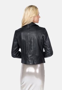 Zwarte leren cropped jacker met een eenvoudige kraag, zichtbare stikseldetails en een gladde textuur. De rug van het model is naar de camera gekeerd.