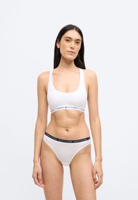 Fehér pamut bralette széles pántokkal, "TOMMY HILFIGER" feliratos szalaggal, és hozzáillő fehér tanga tengerészkék derékpánttal. Sima textúra, testhezálló szabás.