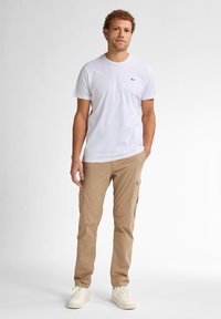 Hvid t-shirt med rund hals og et lille sort logo på venstre bryst, parret med beige cargo-bukser med sidelommer og en afslappet pasform.