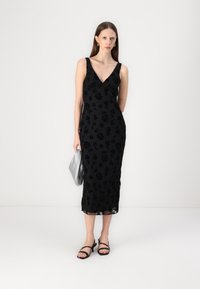 Μαύρο φόρεμα με λουλούδια, με V-λαιμόκοψη, χωρίς μανίκια και μίντι μήκος. Συνδυασμένο με μαύρες σανδάλια με λουράκια και ασημένια τσάντα πορτοφολιού.