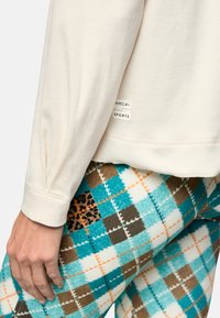 Cream sweatshirt with ribbed texture and logo tag, paired with patterned leggings in turquoise, brown, and orange plaid with animal print accents.