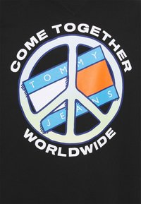 Camiseta negra con un gran gráfico de signo de paz con el texto "UNÁMONOS" y "A NIVEL MUNDIAL", junto con el logo de "TOMMY JEANS" en azul y naranja.