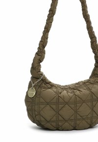 Sac en tissu olive matelassé, de forme courbée, avec une sangle large tressée et un accent en chaîne argentée comportant une étiquette circulaire.