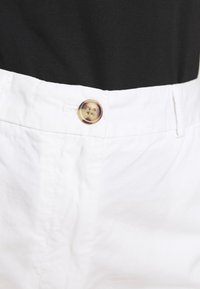 Pantaloni bianchi in cotone caratterizzati da una texture liscia, una chiusura con bottone tradizionale in un motivo tartaruga chiaro e una vita standard.