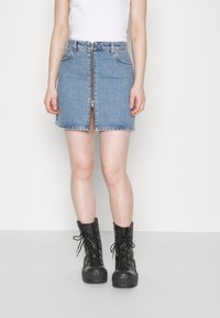 Denim minikjol i ljusblått, med dragkedja fram, fem fickor och rå nederkant. I kombination med svarta snörstövlar med platå.