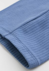Primer plano de una suave tela de ribete azul doblada, con líneas de costura visibles a lo largo de los bordes, sobre un fondo claro.