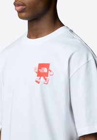 Bílý bavlněný tričko s červenou grafikou čtvercového charakteru s rukama a nohama, umístěným na levé části hrudi.