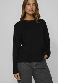 Pull noir en tricot côtelé, avec un col rond, des manches longues et des détails de couture subtils sur le devant.