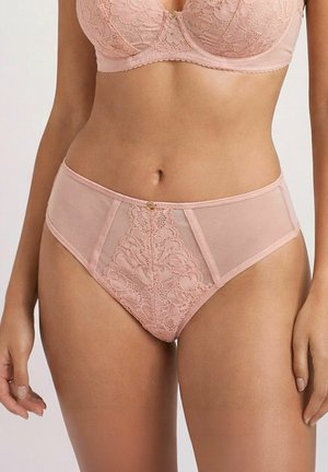 Kobieta w dopasowanym bladoróżowym koronkowym staniku i majtkach z wysokim stanem z kwiatowymi wzorami, pokazana od połowy torsu do górnej części ud.