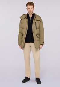 Olivově zelená vyplněná bunda s kapucí, předním zipem a klopovými kapsami. Nosená přes černý top, spárovaná s béžovými kalhotami a černými botami.