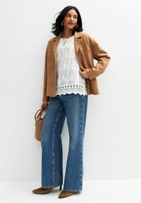 Tansuede blazer over een witte kantentop met geschulpt zoom, gecombineerd met een wijde blauwe denim jeans en bruine pumps met een spitse neus. Geweven handtas.